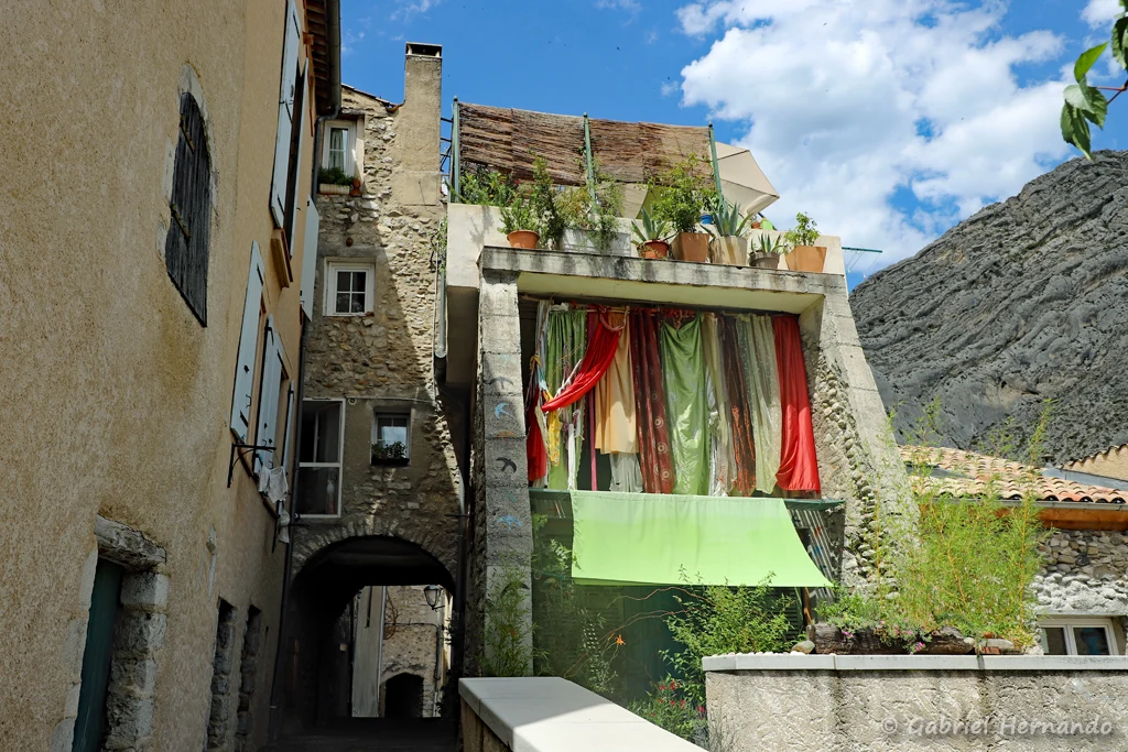 Passage couvert et ruelle de la ville, avec une maison parée d'un patchwork de rideaux